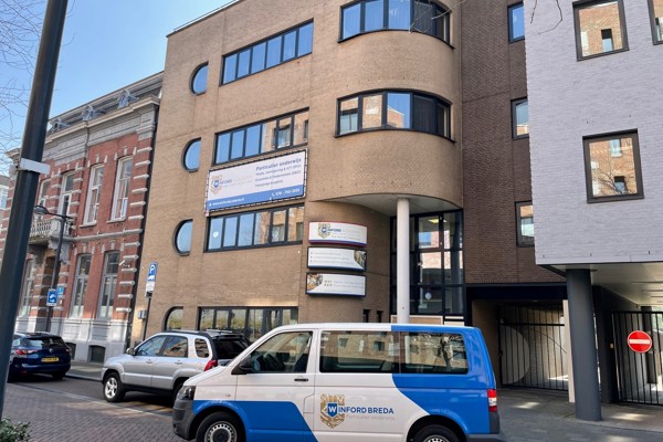 Het schoolgebouw in Breda aan het stationsplein met een busje ervoor.